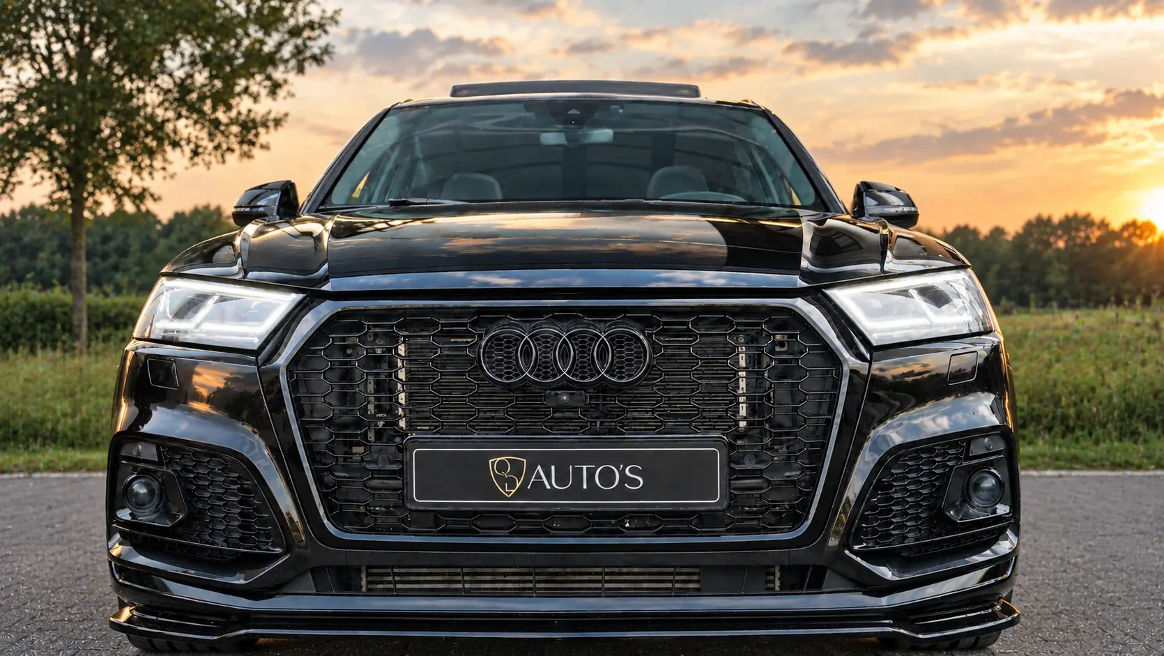 Vooraanzicht van een zwarte Audi met kentekenplaat van QD AUTO'S bij zonsondergang