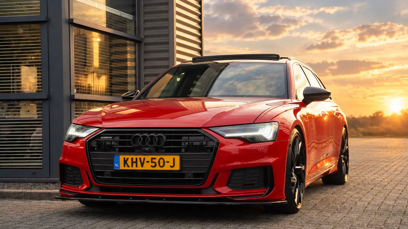 Rode Audi A6 Avant bij zonsondergang voor de showroom van QD AUTO'S